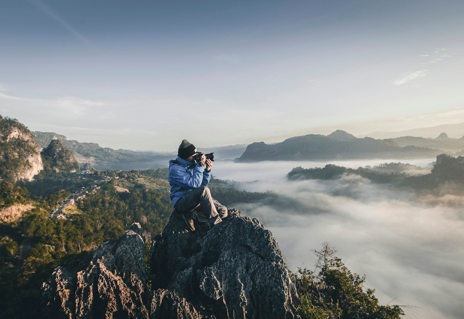 Photographer sitting on a rock ridge above a valley filled with morning cloud