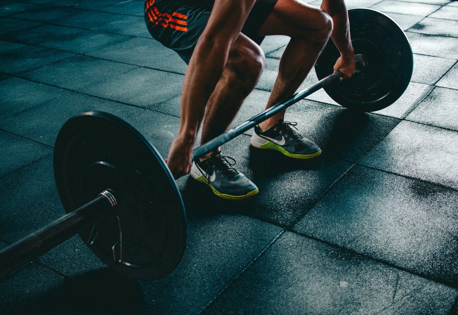 Athlete holding a barbell on a black gym floor, training shoes planted