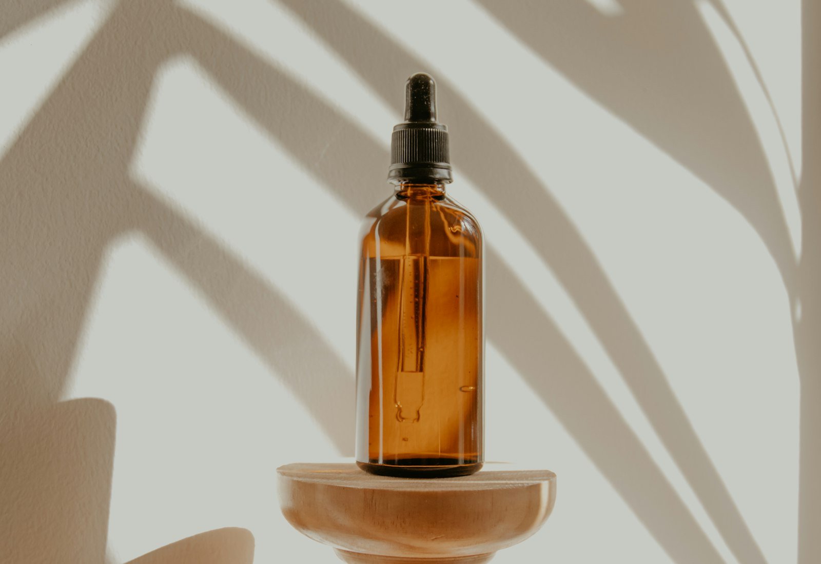 Amber glass dropper bottle on a wooden stand, leaf shadows on a pale wall